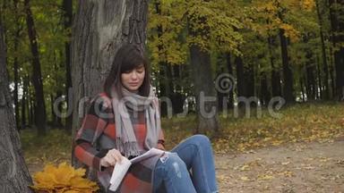 从<strong>笔记</strong>本上取一片叶子。 在公园里的草地上坐着一位迷人的年轻快乐的微笑女人，在<strong>笔记</strong>本上记<strong>笔记</strong>